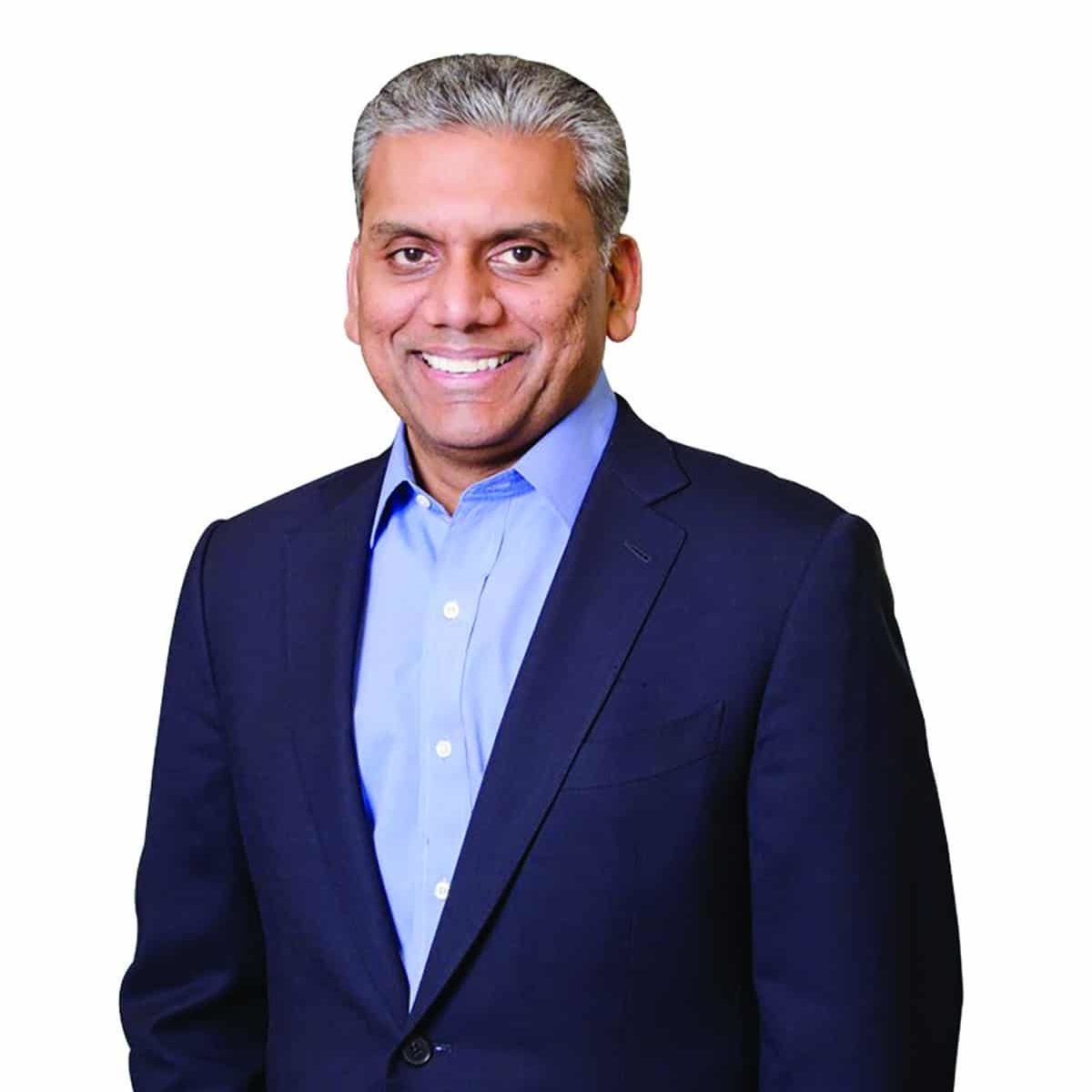 Anurag Jain Anurag Jain smiling in a dark suit and blue button down shirt in front of a white background