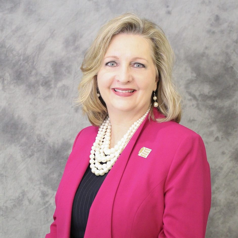Trisha Headshot Trisha Cunningham in a pink blazer and pearl necklack against a grey background